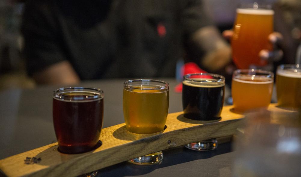 A flight of beers is served at the bar.