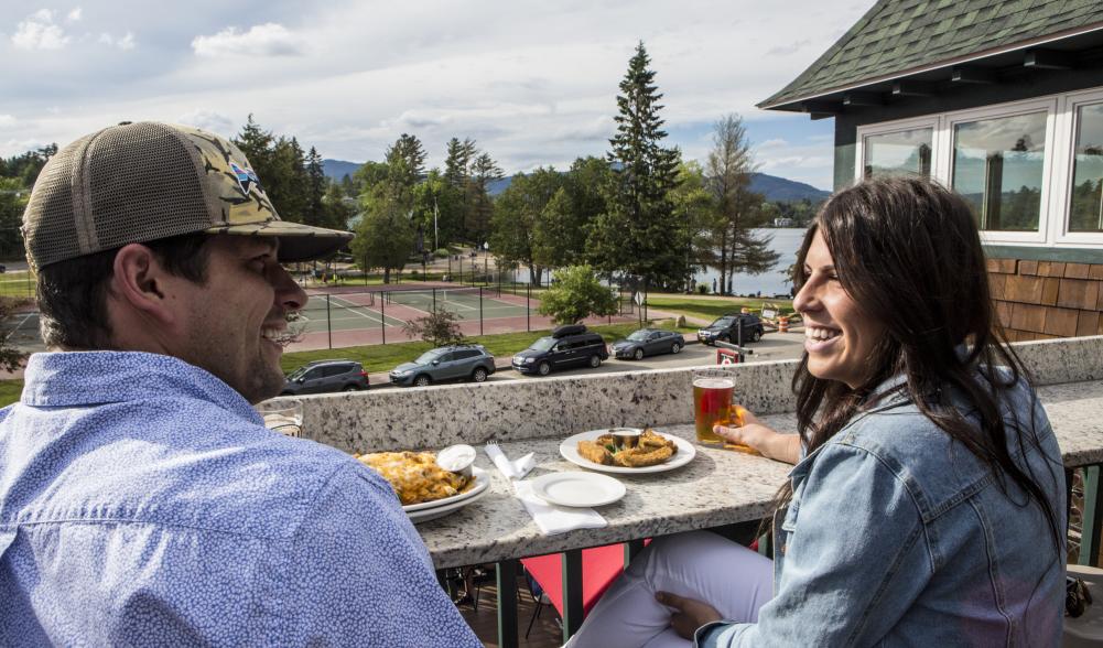 A couple smiles as they enjoy a meal on an outdoor deck.