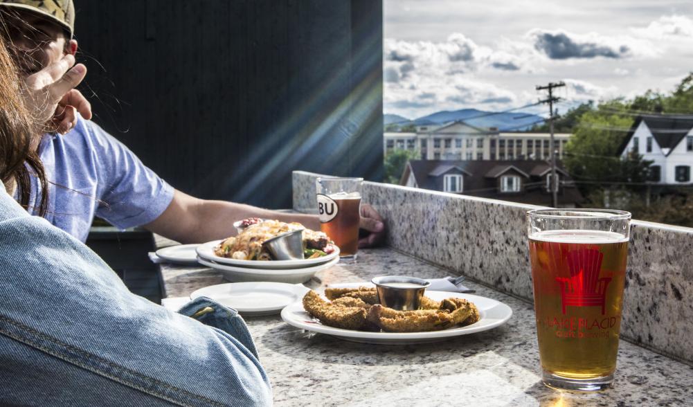 A couple eats on an outside deck with a view of the mountains in the background.