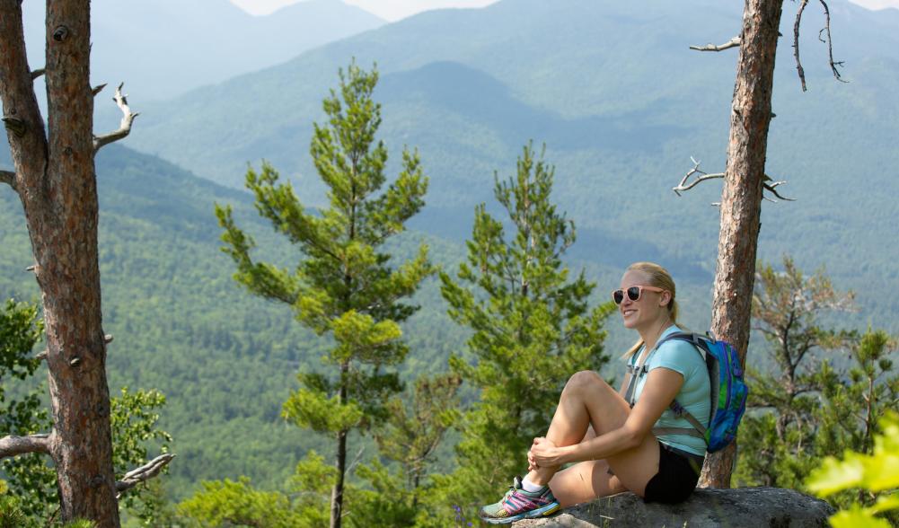 A woman sitting on a rock on top of a mountain overlooking the peaks in the distance.