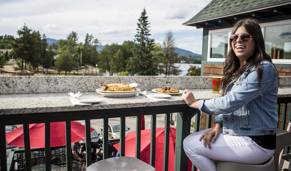 woman dining outside overlooking trees and a lake.