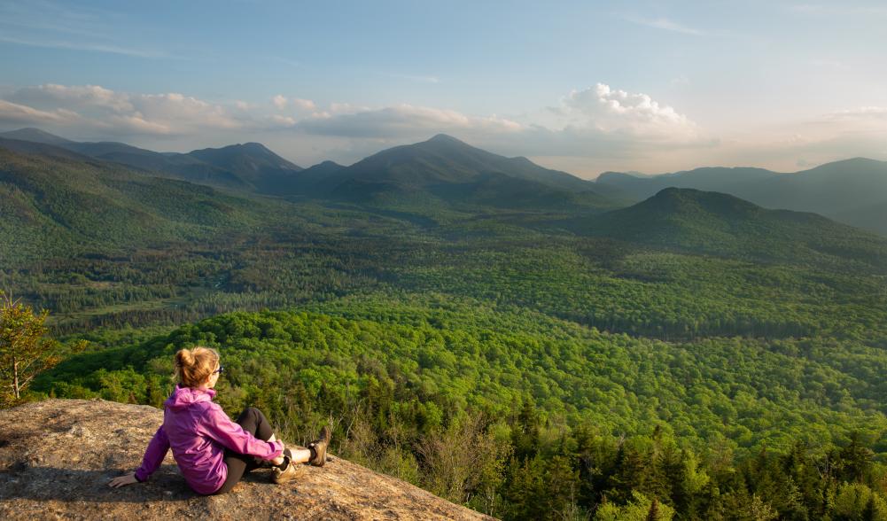 A hiker sits atop a rock, overlooking the mountain range.