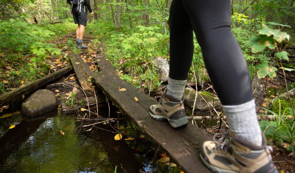 A hiker crosses a creak on a plank of wood.