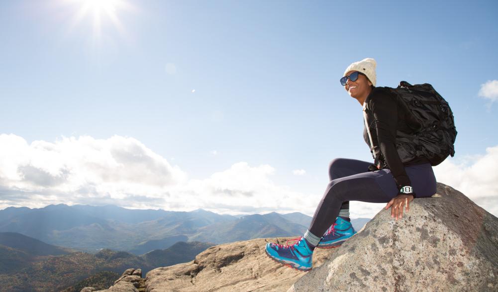 A woman sits on top of a rocky mountain, overlooking the mountain range.