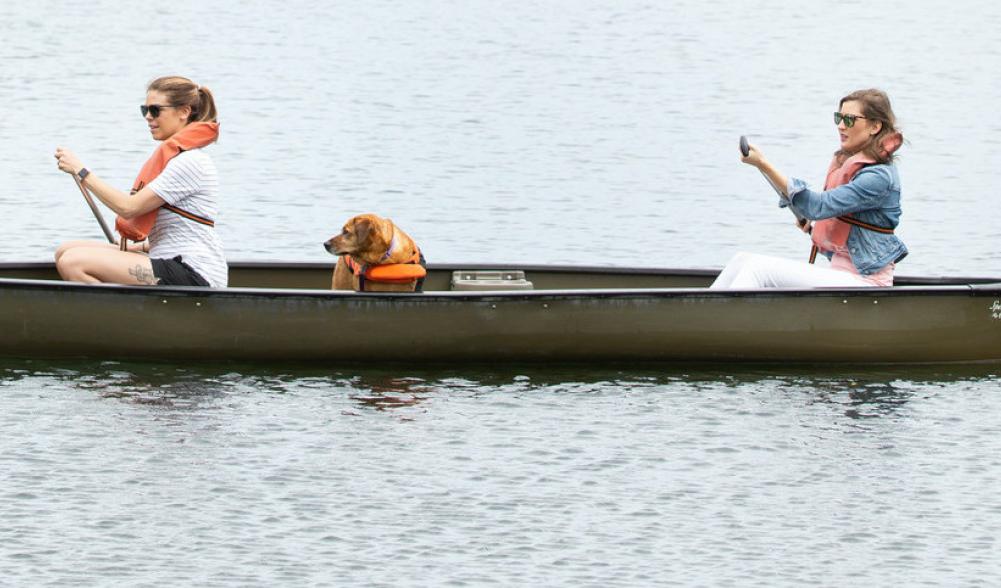 Two women and a dog in a brown canoe.