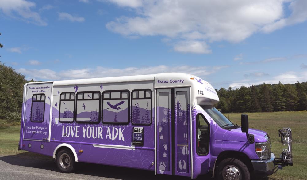 A side view of the purple, ADK-themed hiking shuttle bus.