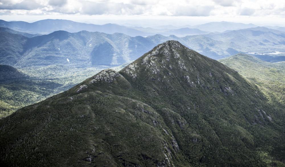 An aerial view of the towering High Peaks, with rocky summits and forested slopes.