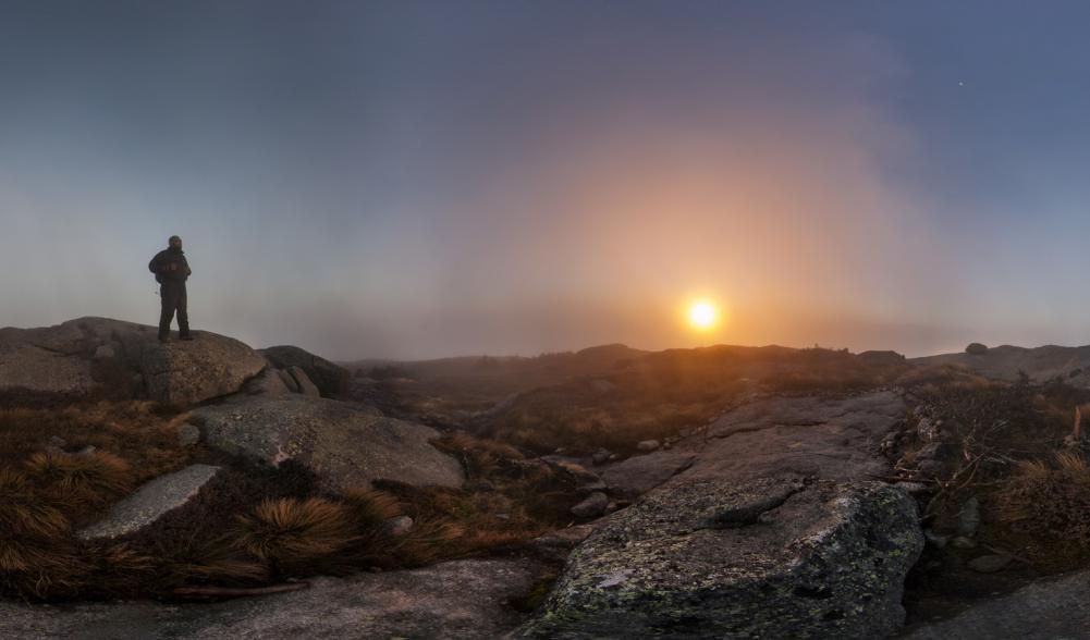 A hiker standing on a mountain summit during a foggy sunrise.