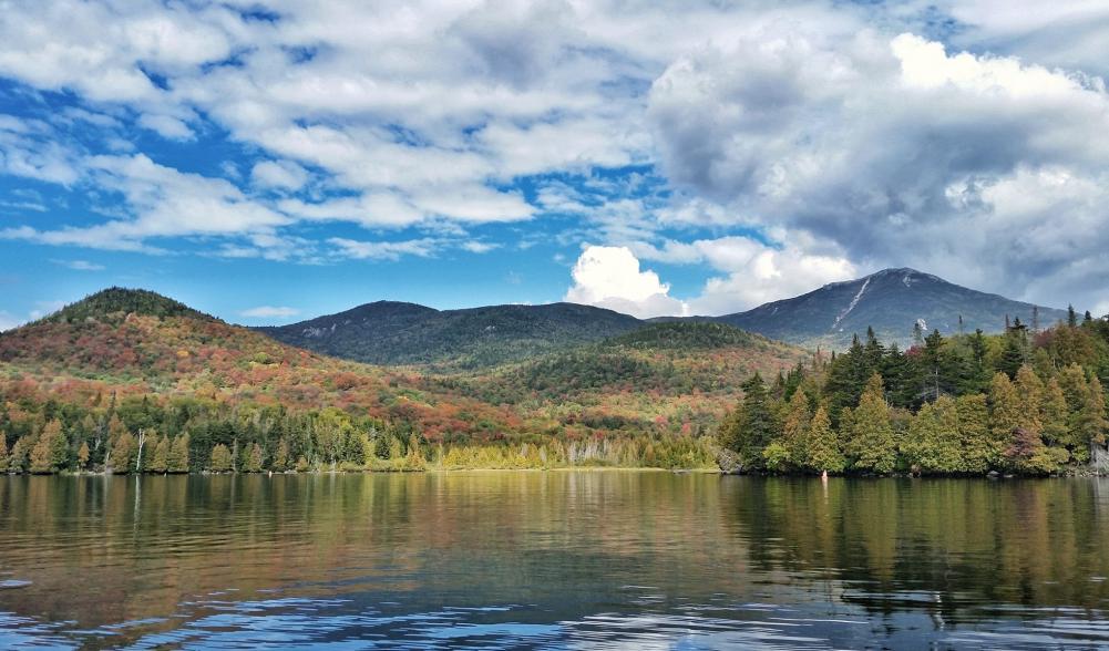 Calm waters and fall colors from a boat in Lake Placid. The trees are starting to turn red.