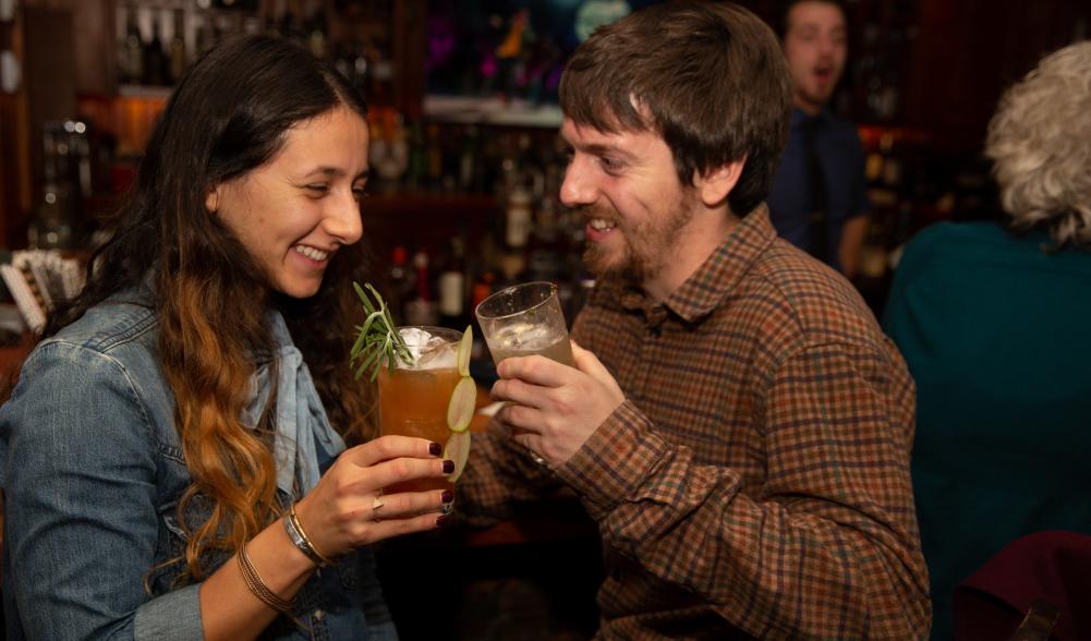 A couple holds cocktails at a bar.