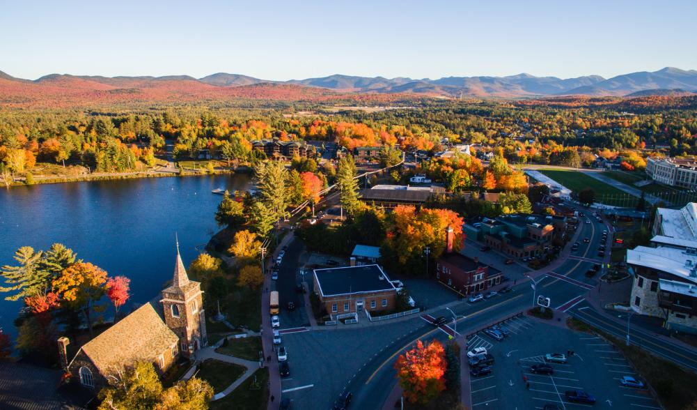 Aerial view of Lake Placid. Trees with fall foliage. Main street. Mirror Lake. Mountains in the background.