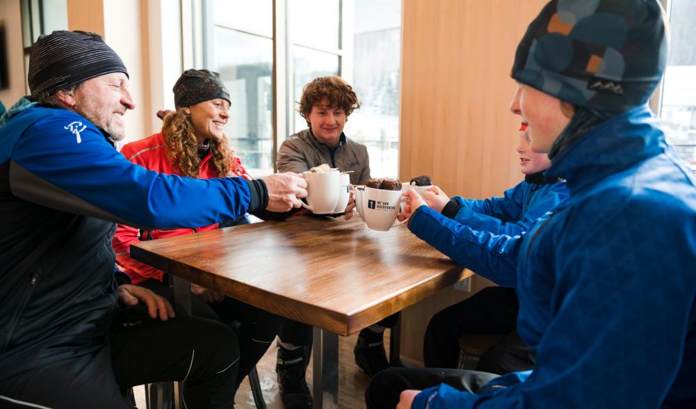 A family drinks hot cocoa at a table next to a snowy window.