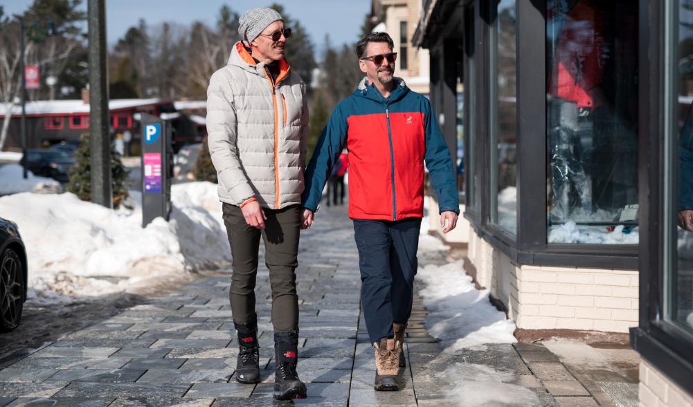 Two men walk on Lake Placid Main Street in winter on a sunny day.