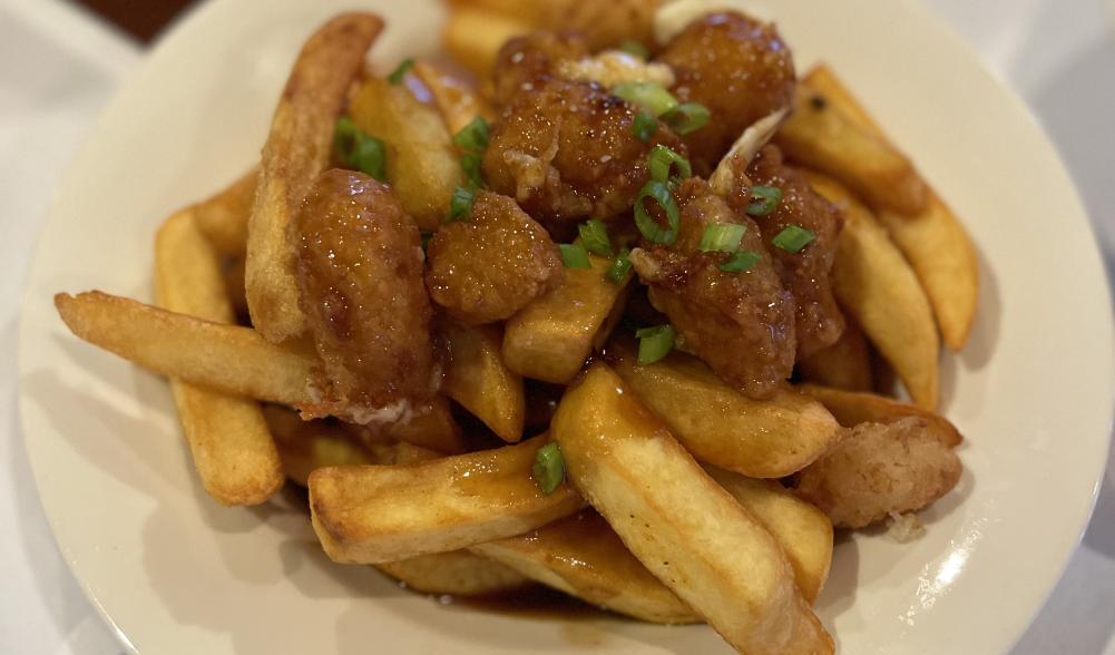 Extreme close-up of a dish of glazed, fried cheese curds on a bed of French fries.