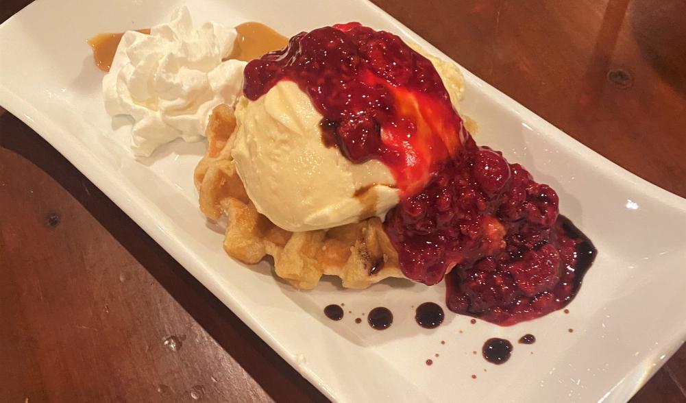 A lavish dessert of waffle, ice cream, caramel, and raspberry sauce.