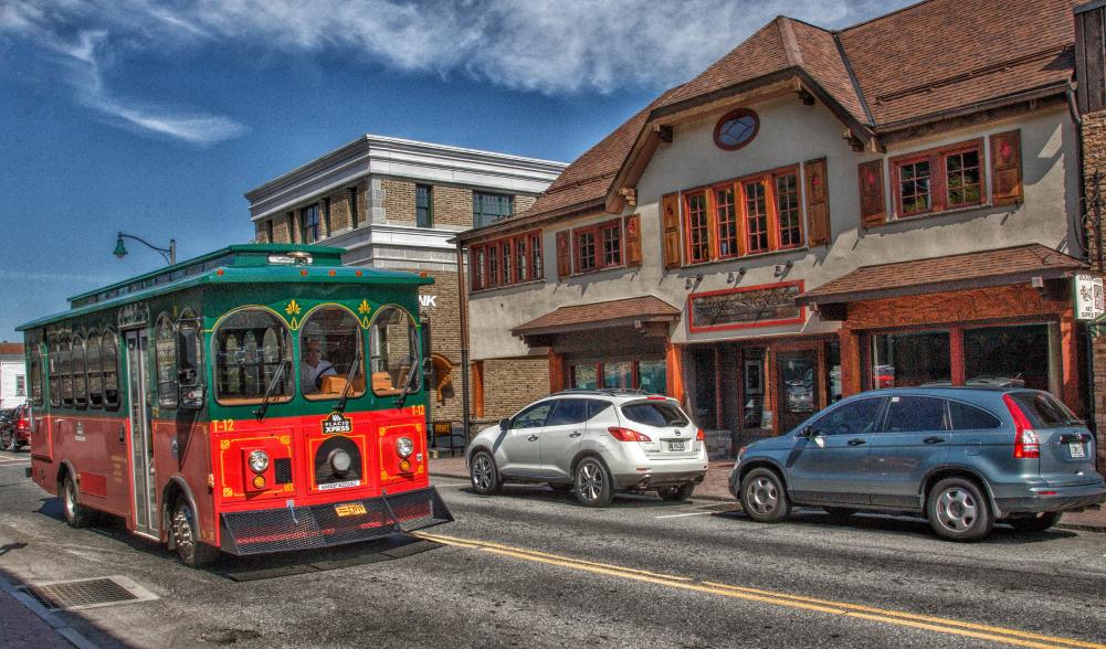 A trolley bus drives on a quaint street past a barbecue restaurant.