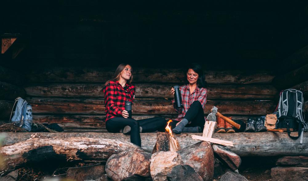 Two women in flannels talk in a lean-to.