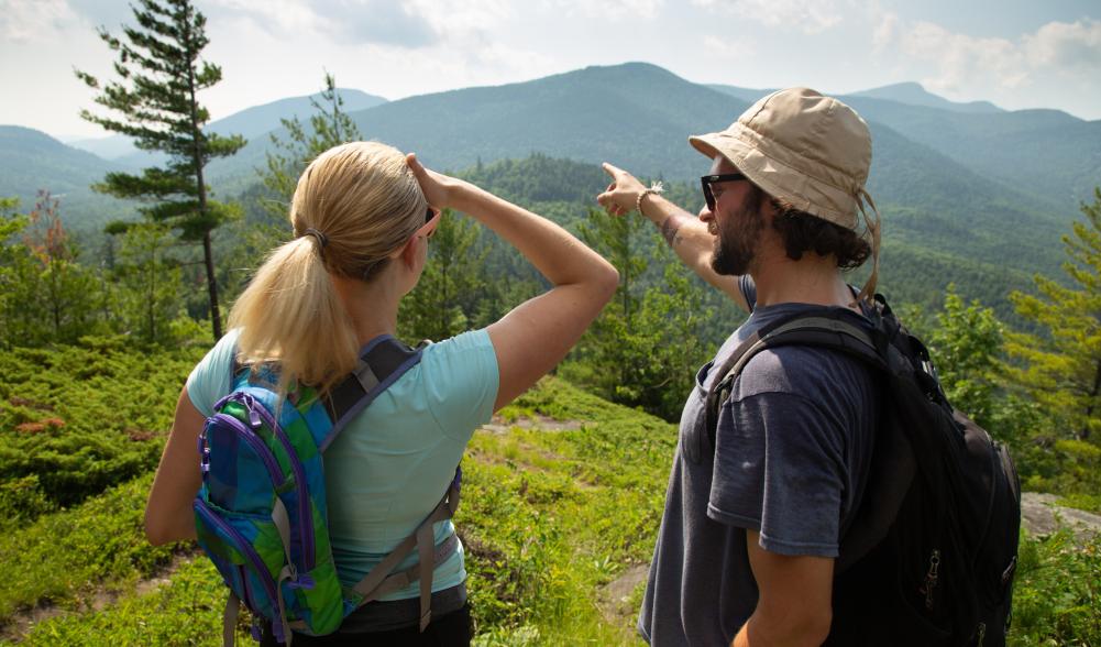 A man shows a woman the view of a mountain in the distance.