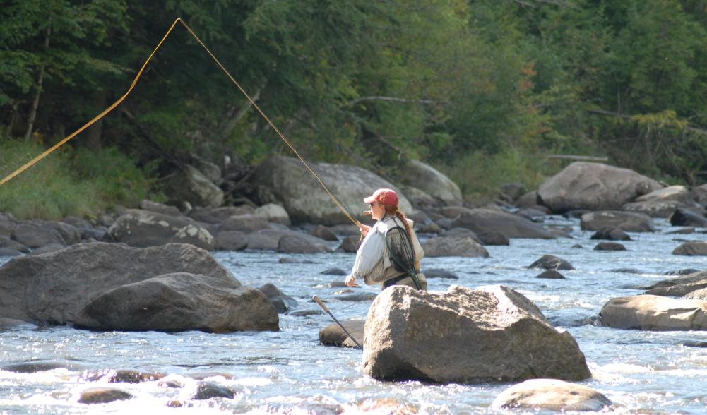 A woman casts a fly fishing lure in a stream.