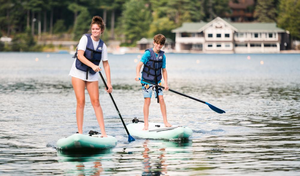 Two kids paddle on SUPs on Lake Placid.