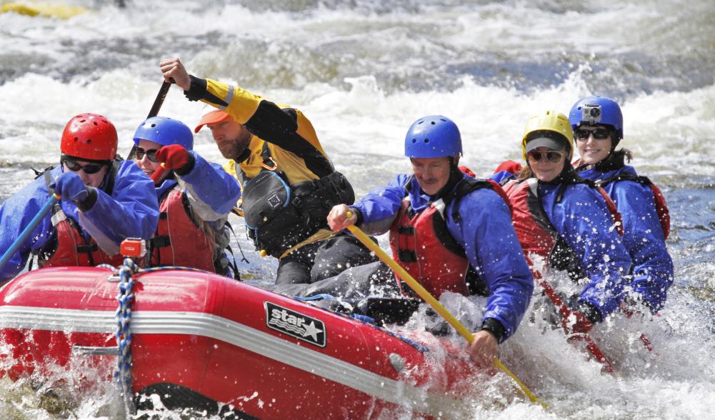 A group paddles through rapids on a group raft.