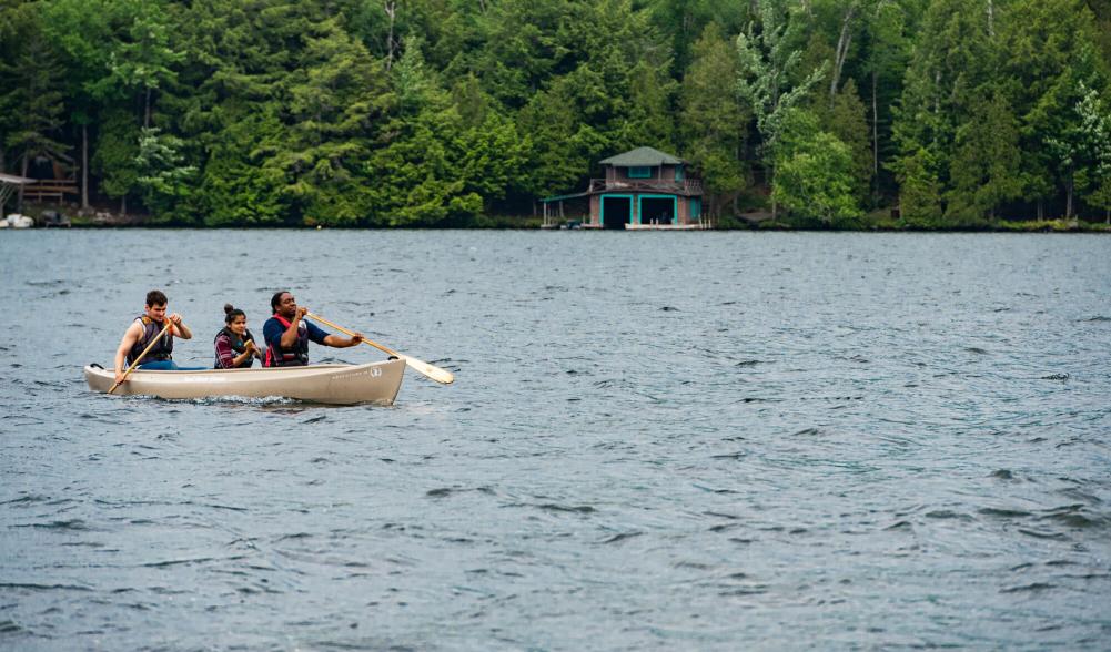 A man paddles with two passengers in a canoe.