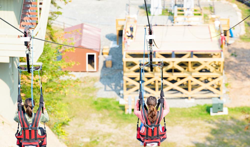 two women ride a zipline down to a platform.