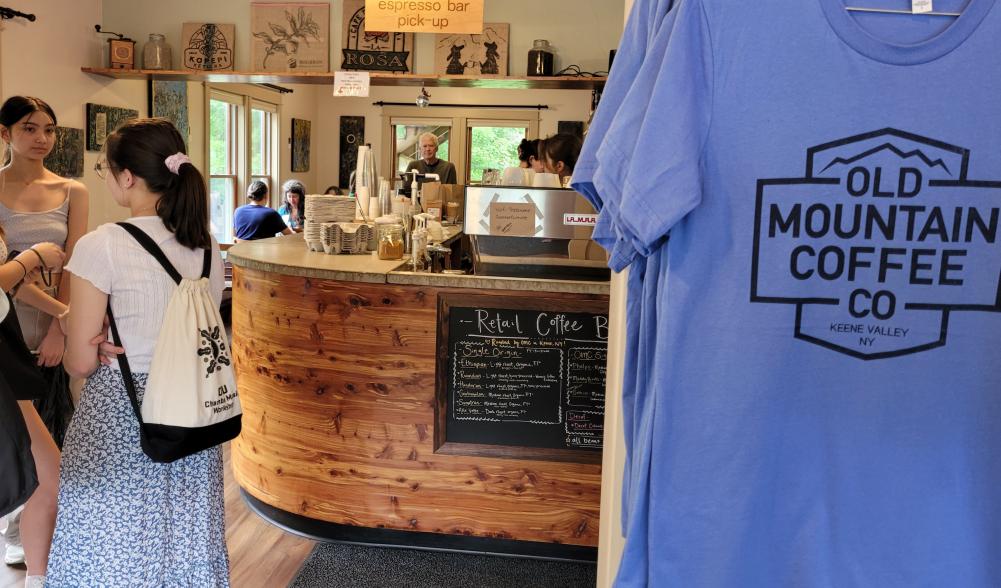 The interior of Old Mountain Coffee with a pastry case, people in line and a blue t-shirt with the company logo
