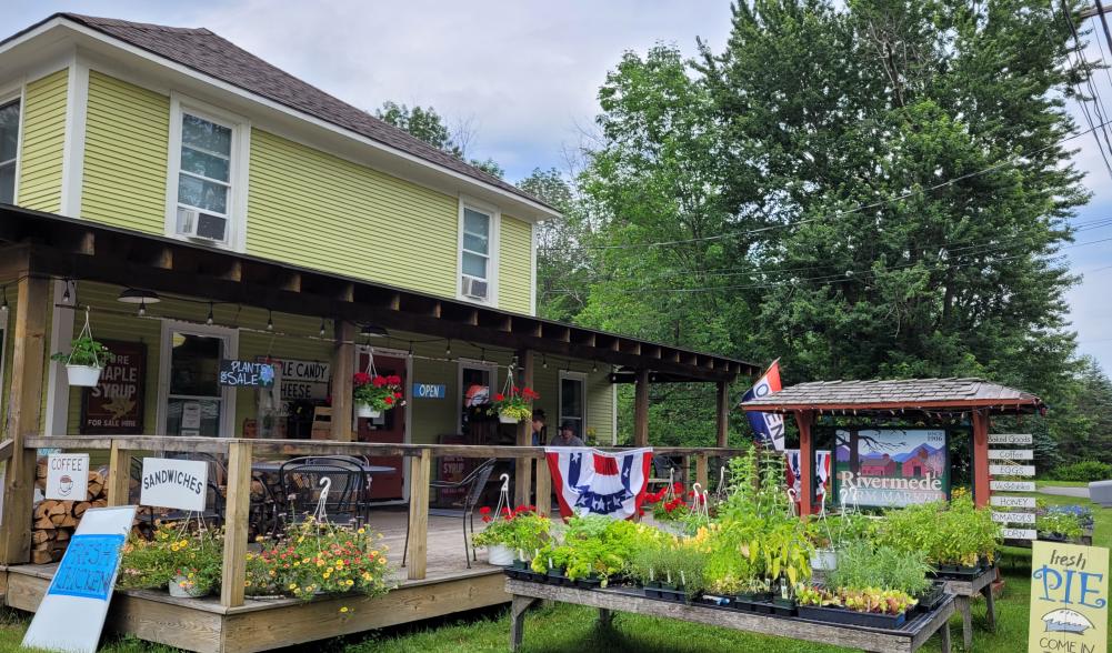 Rivermede Farm Market is a yellow building with a big front porch. Two men and their dog are on the front porch