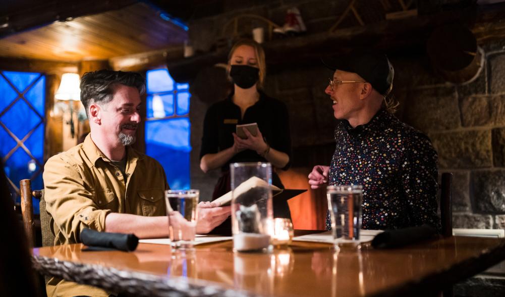 Two men smile while ordering food at a romantic, dimly lit restaurant.