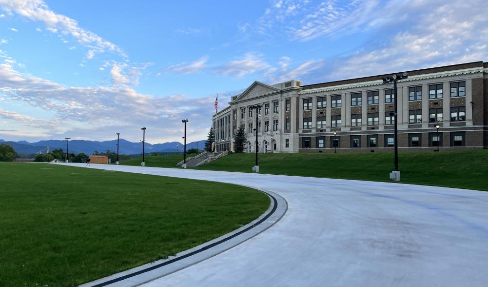 A stone high school overlooks a smooth skating track on a summer day.