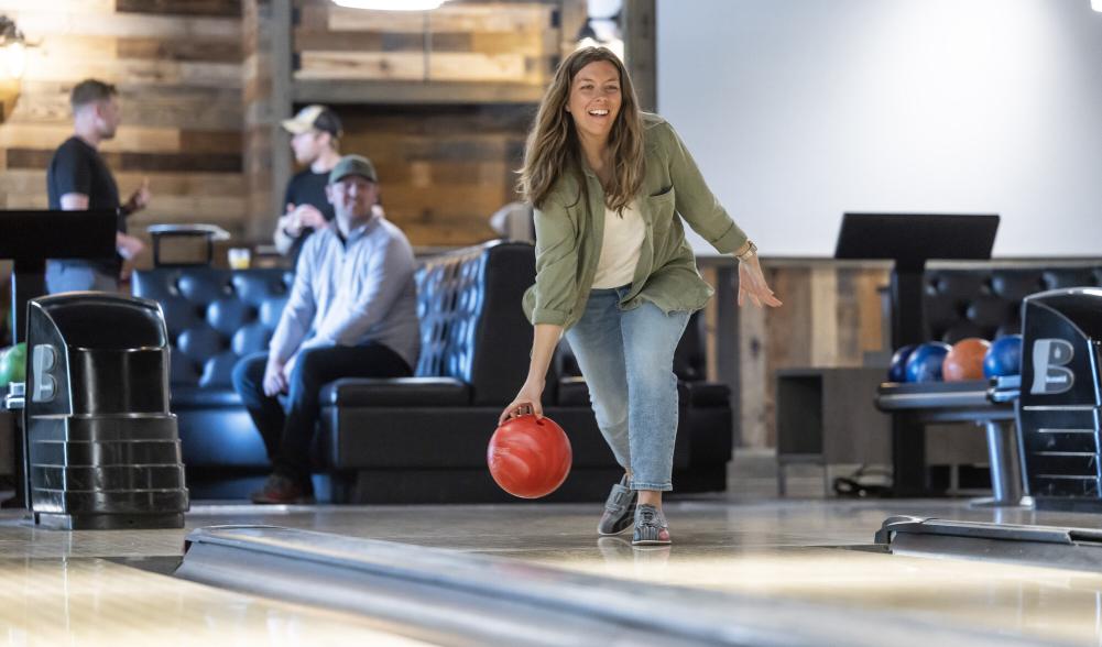 A woman prepares to release a bowling ball on a wood alley at a hip bowling alley.