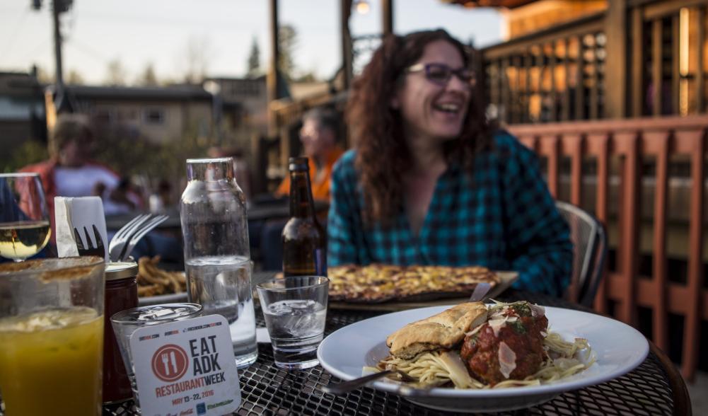 A woman laughs with food on a patio.