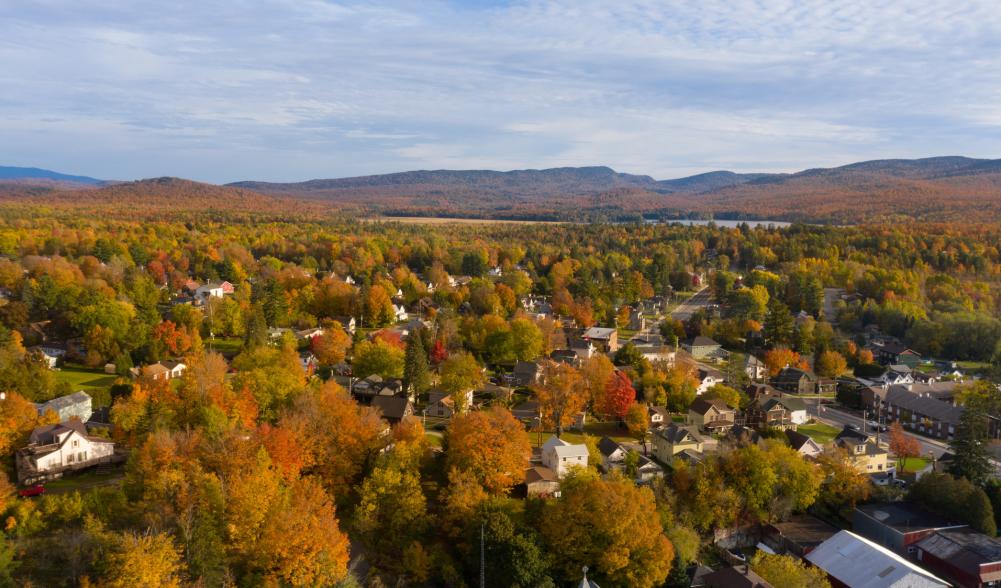 Downtown Tupper Lake with mountains in the back covered in fall reds and yellows.