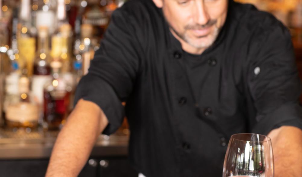 A man stands at a bar with tuna and a drink.