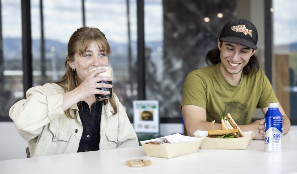 A man and woman enjoy coffee and sandwiches on a deck.