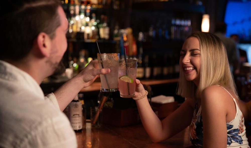 A man and woman share drinks at a bar.