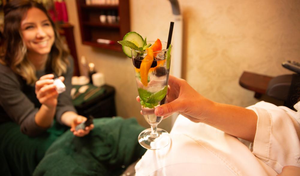 A woman's hand holds a mineral water adorned with a fresh citrus wedge in a Lake Placid spa