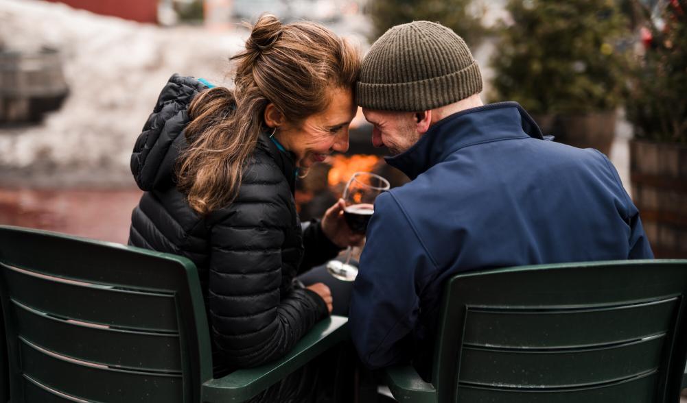 A man and woman share wine in Adirondack chairs.