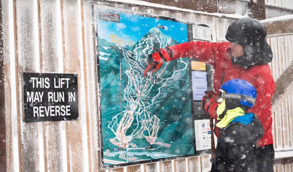 A father pointing out something on a ski mountain map to his kid