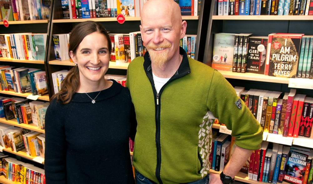 The owners of The Bookstore Plus stand in front of a display of books in their store