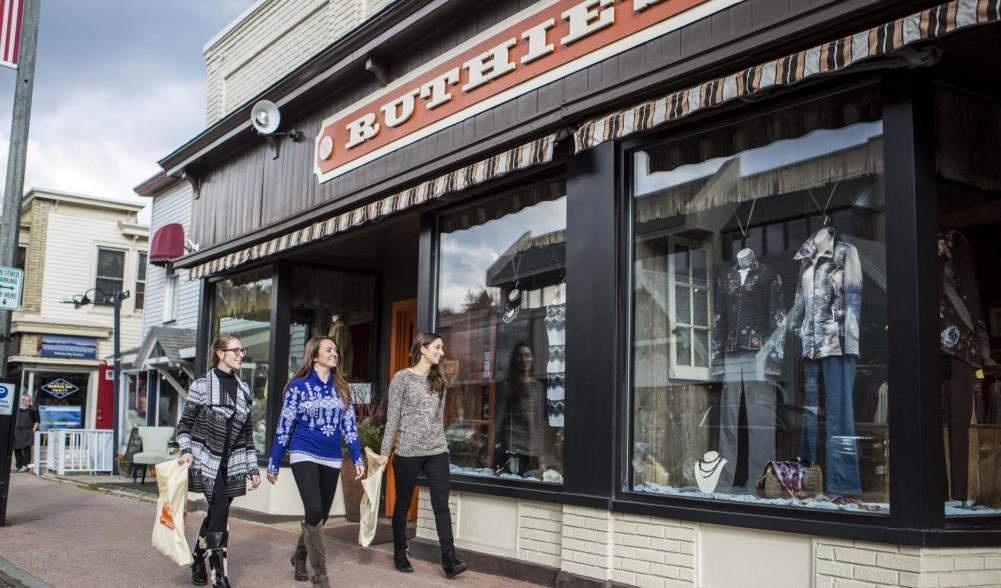 Three people walk on the Lake Placid sidewalk carrying shopping bags