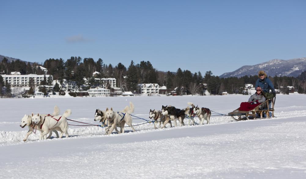 A couple rides in a dog sled on a frozen lake.