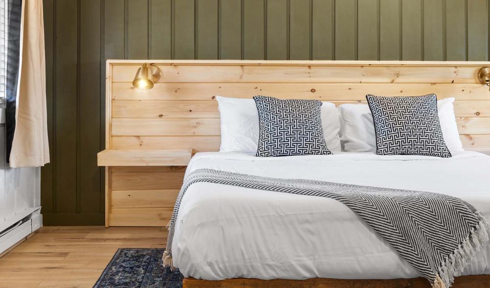 A white bed next to a green wall in a simply decorated room.