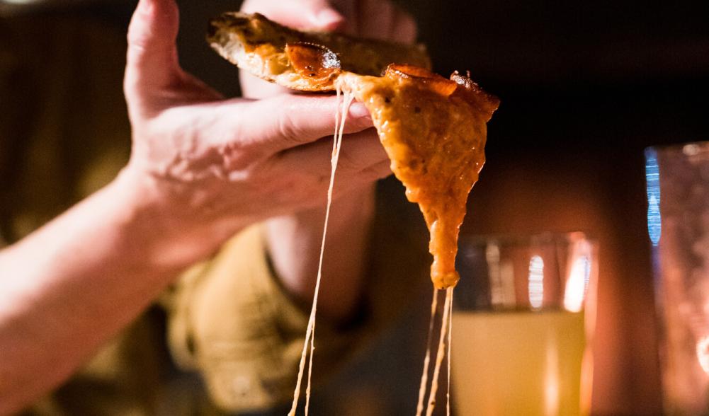 A man's hand holds a slice of wood-fired pizza