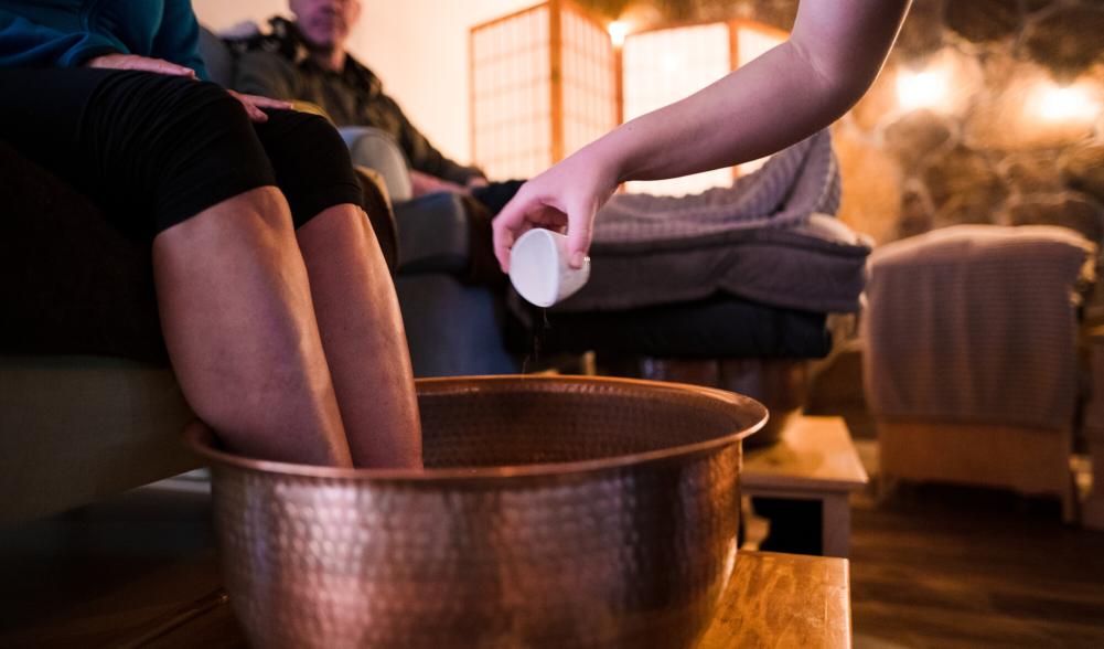 A person soaks their feet in a large copper kettle at The Adirondack Foot Sanctuary
