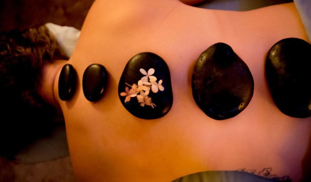 A woman lies on a spa table with hot stones in a line down her back.