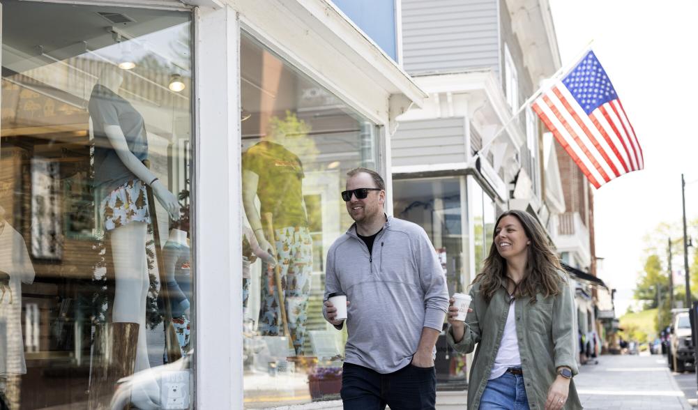 A man and woman wear spring-time outfits and window shop down Main Street.