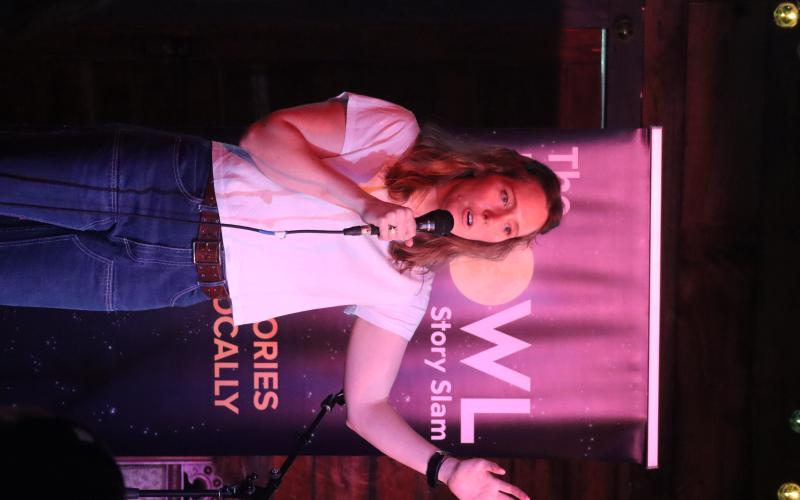woman stands holding hand up speaking into microphone