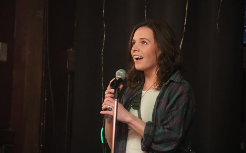 woman stands on stage talking into microphone